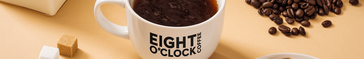 Eight O'clock coffee in a mug with scattered coffee beans and golden spoon on the side.